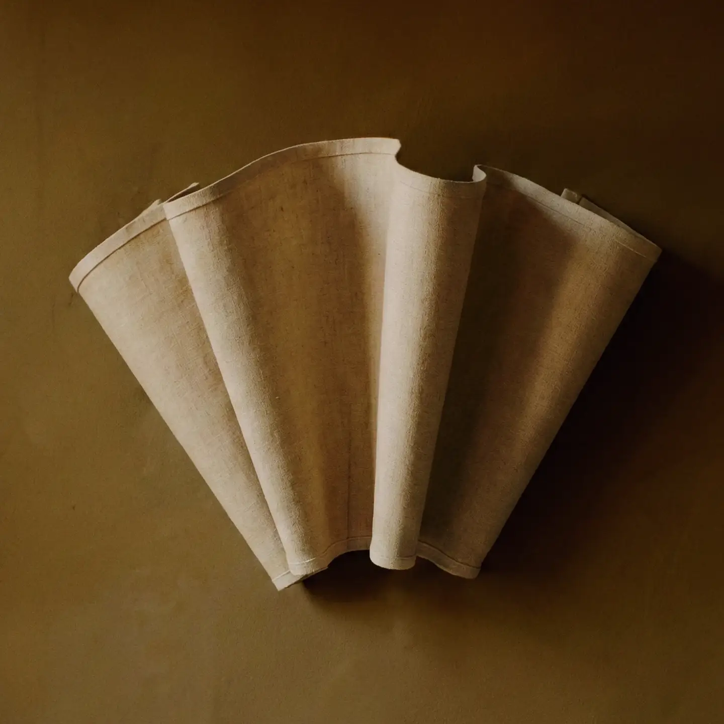 Feuillet wall lamp with a fluted, fan-shaped linen shade mounted on an olive wall